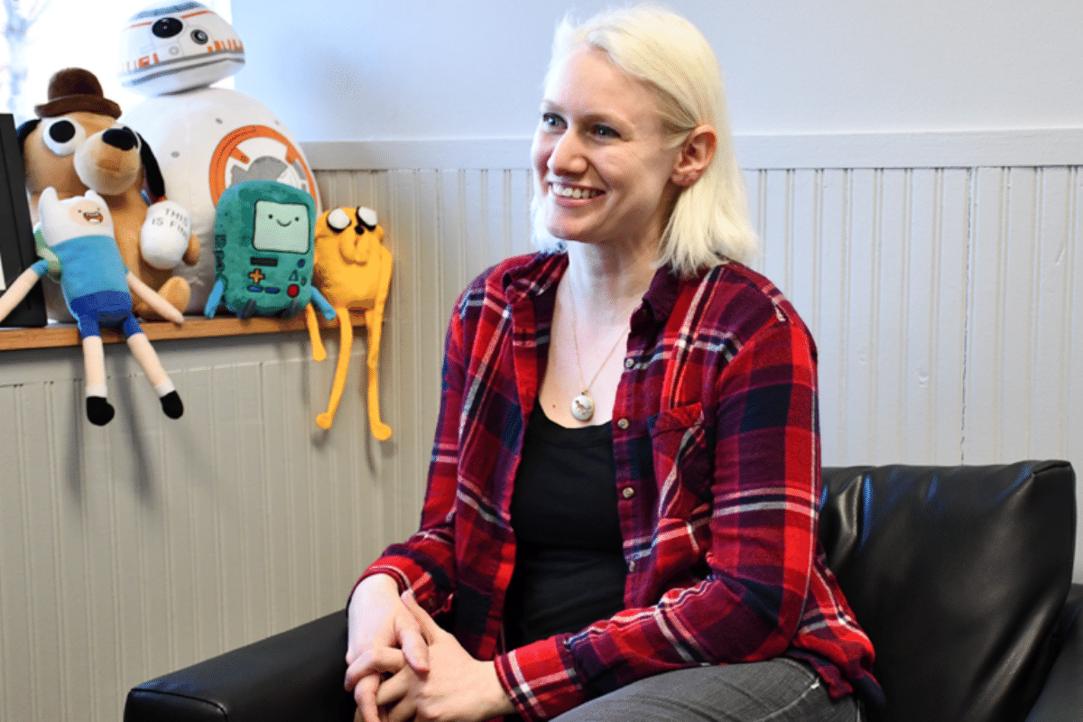 Justine sits in her office, smiling at client, with fandom-centric plush characters in the background.