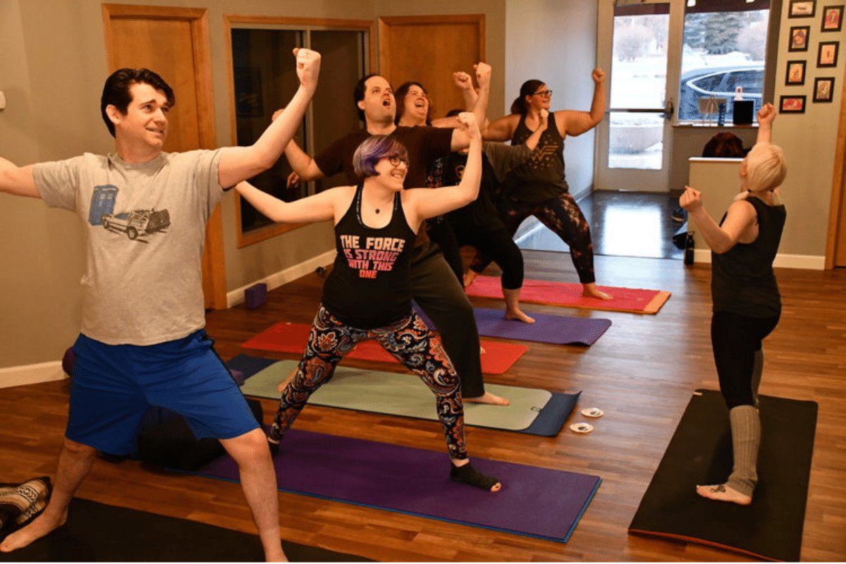 Yogis demonstrate Warrior 2 pose with arms raised in battle.